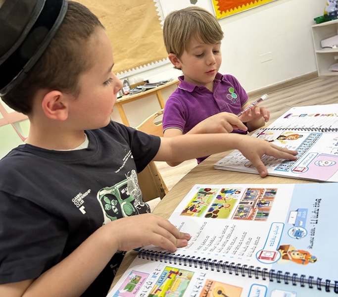 Young boy pointing at an illustrated Hebrew learning workbook