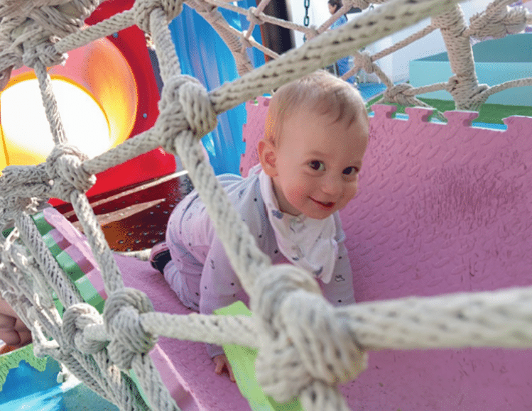 Baby smiling in a hammock at a colorful indoor play area