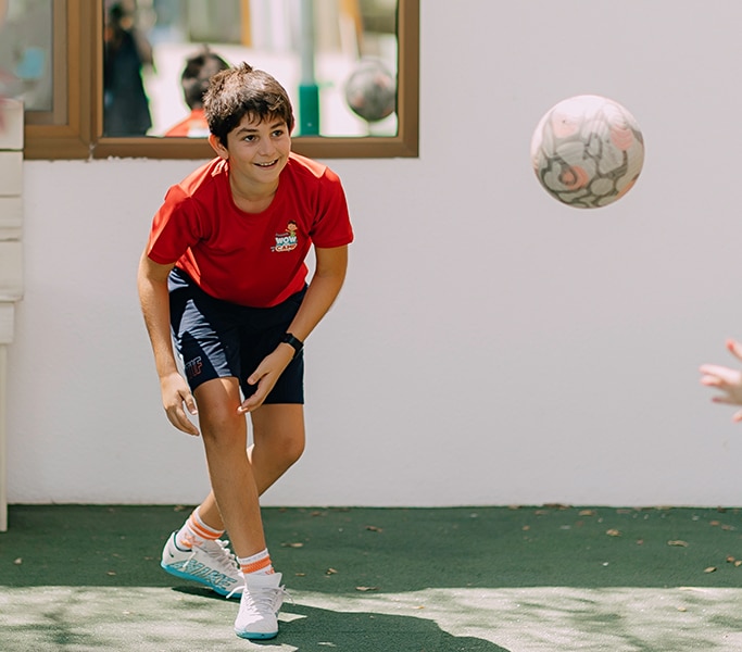 Girl in red sports shirt kicking a soccer ball outdoors